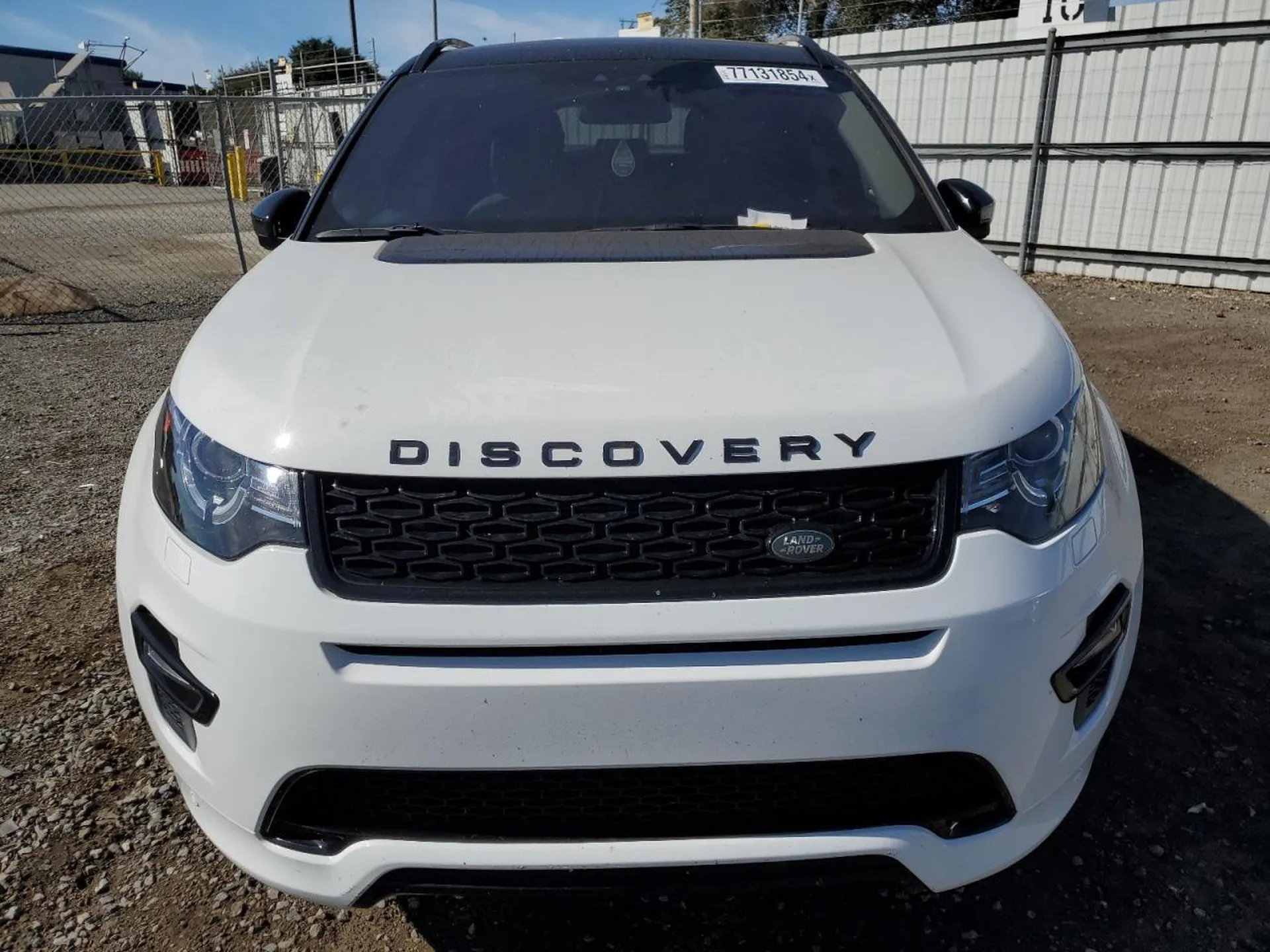 Przód białego Land Rovera Discovery Sport z napisem DISCOVERY na masce i reflektorami LED.