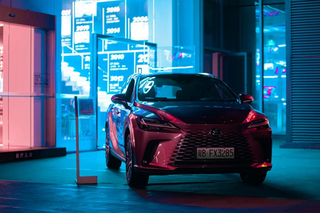 Czerwony Lexus NX zaparkowany nocą przed nowoczesnym budynkiem oświetlonym neonami