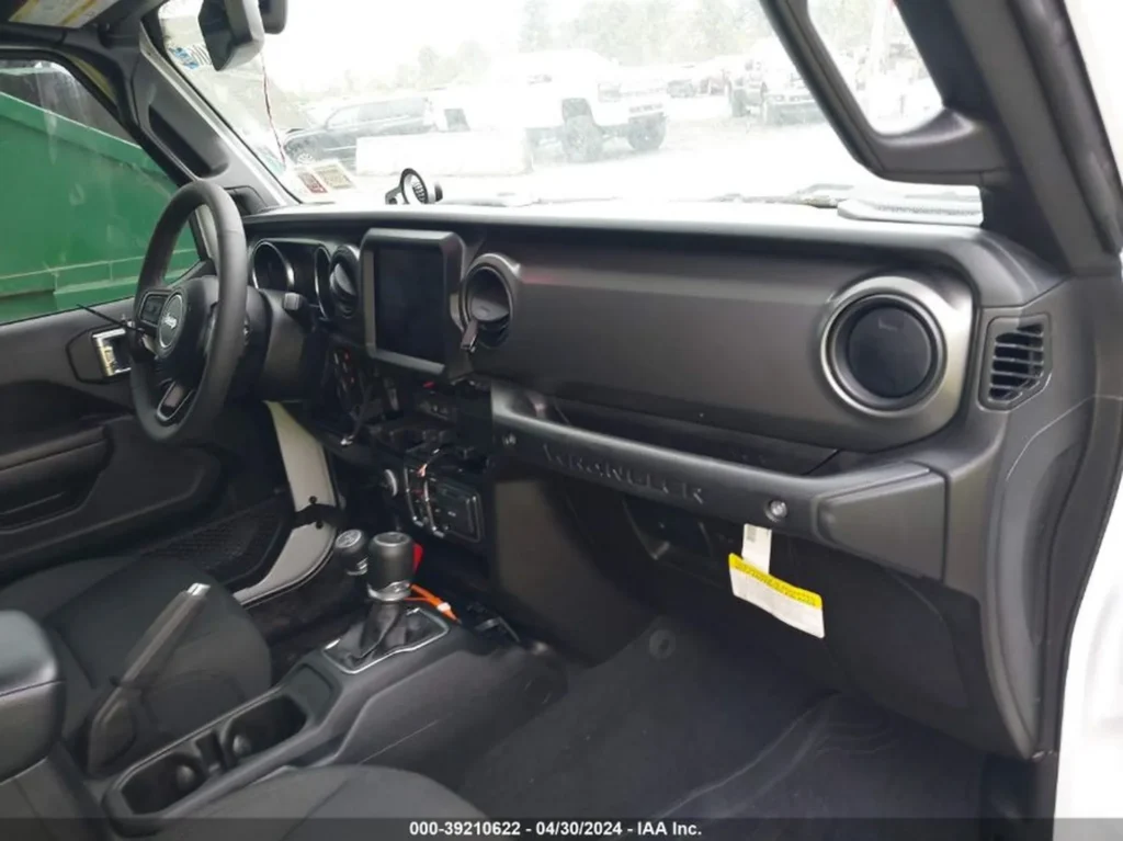 Wnętrze Jeepa Wrangler 4xe; deska rozdzielcza z ekranem infotainment i uchwytem „WRANGLER”, manualna dźwignia 4x4.