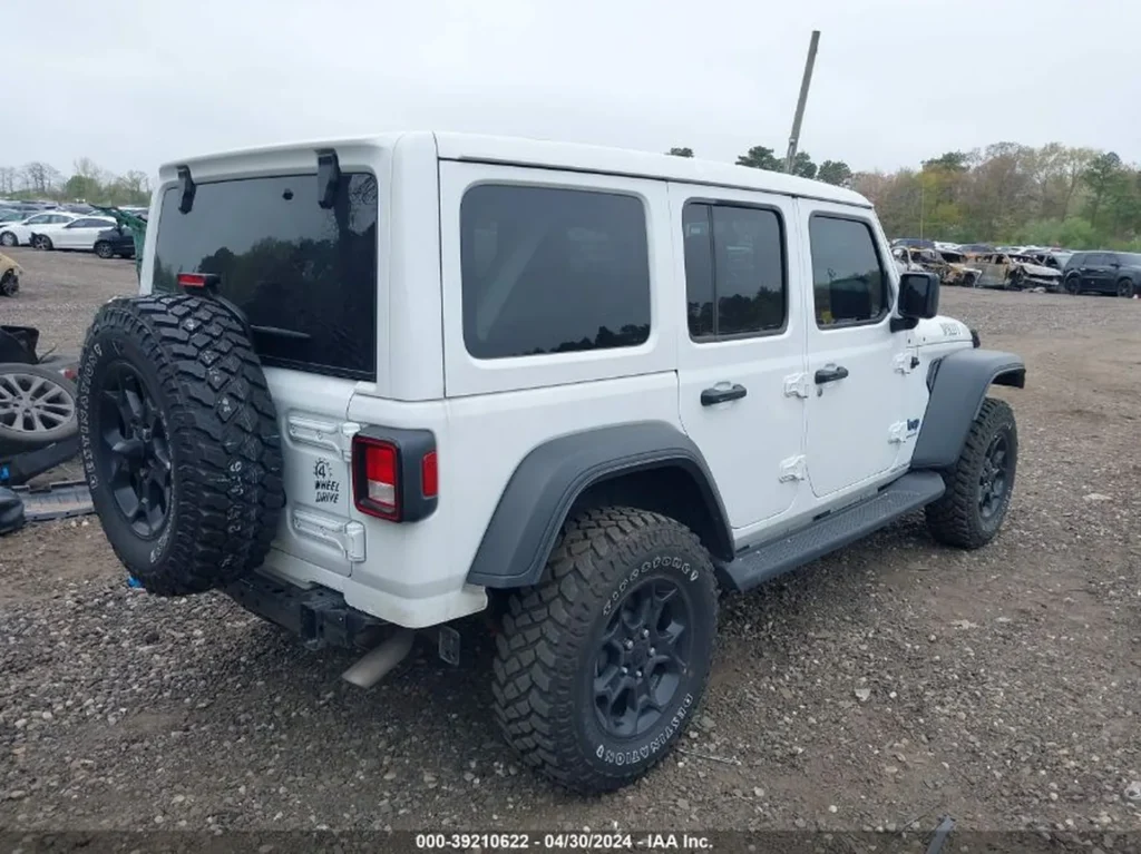 Tył i lewa strona Wrangler Willys 4xe na szutrze; koło zapasowe, czarne felgi terenowe.