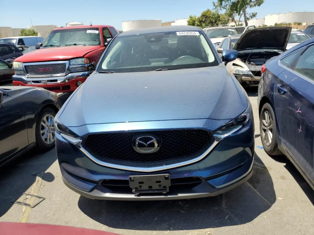 Ujęcie frontalne Mazdy CX-5 na zatłoczonym placu; grill z logo Mazdy, reflektory LED.