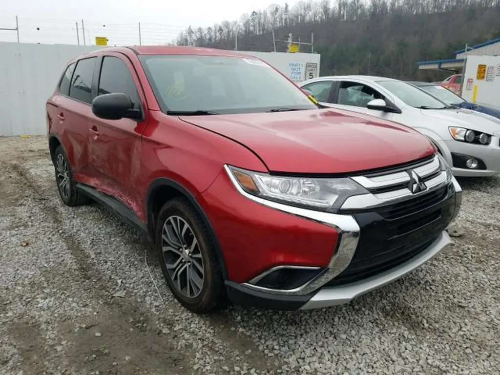 Czerwony Mitsubishi Outlander z uszkodzeniami lewego boku, widok z przodu-lewego narożnika na żwirze.