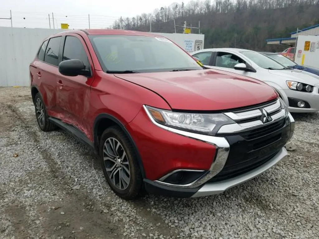Czerwony Mitsubishi Outlander z uszkodzeniami lewego boku, widok z przodu-lewego narożnika na żwirze.