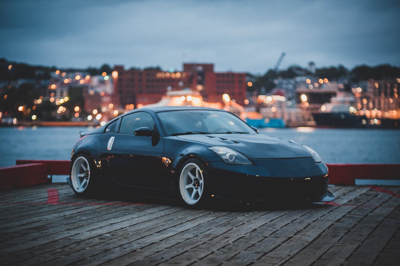 Sportowy Nissan 350Z stoi na nabrzeżu nad wodą o zmierzchu, z miejskimi światłami w tle.