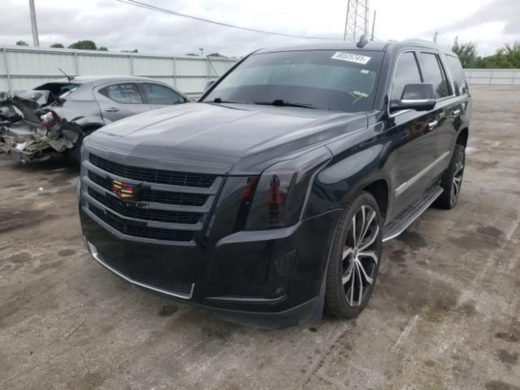 Czarny Cadillac Escalade zaparkowany na placu samochodowym obok uszkodzonych pojazdów