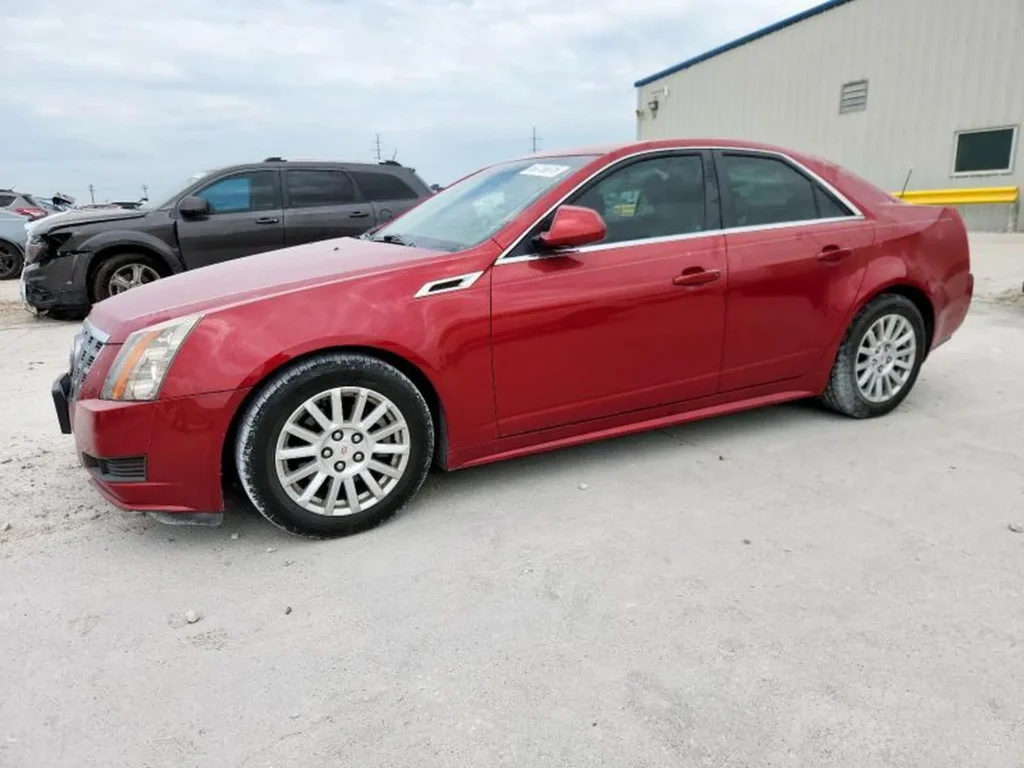 Czerwony Cadillac CTS sedan z boku, auto na placu, koła i progi lekko zakurzone.