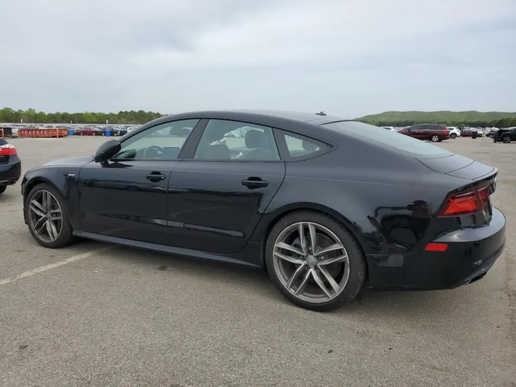 Czarny Audi A7 Sportback - widok z boku na dużym parkingu.