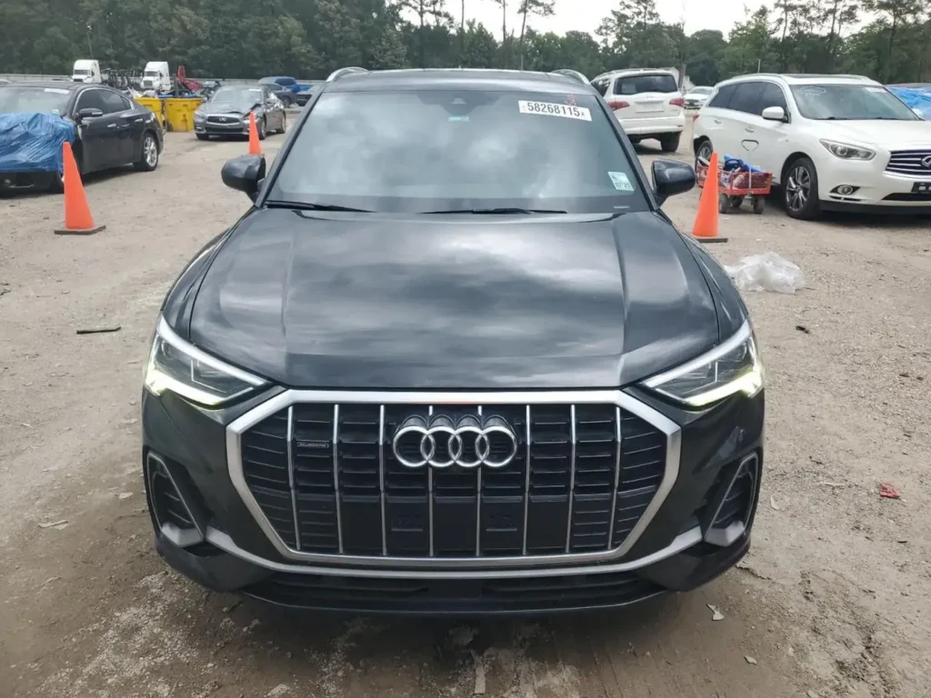Przód czarnego Audi Q3 z włączonymi światłami LED na placu z samochodami