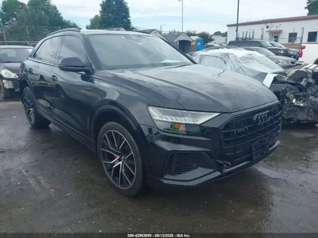 Audi Q8 w czarnym kolorze, widok z boku pod skosem na mokrym parkingu