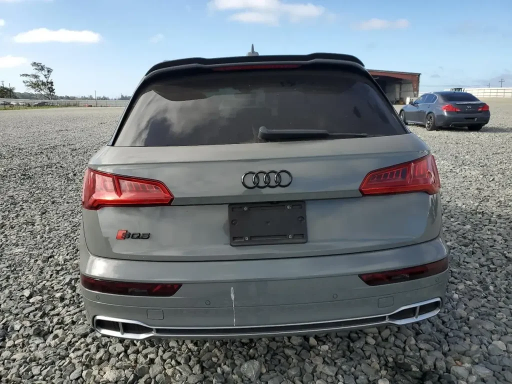 Tył szarego Audi SQ5 z emblematem S i podwójnymi końcówkami wydechu na kamienistym placu