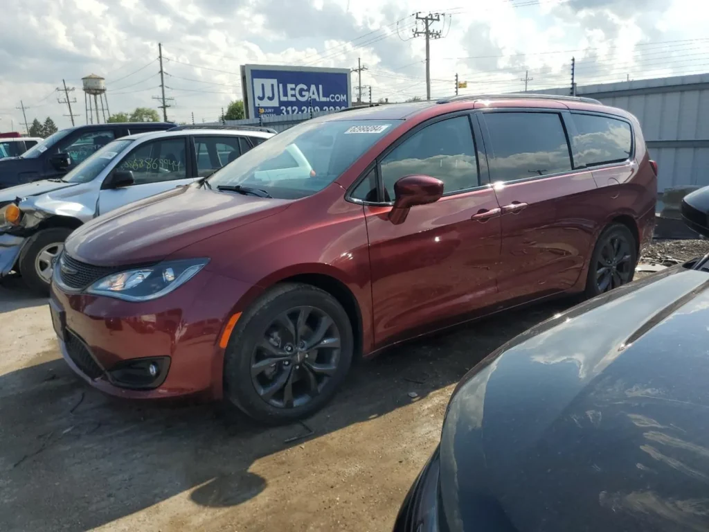 Czerwony Chrysler Pacifica z przyciemnianymi szybami, widok z przodu i boku na placu z autami.
