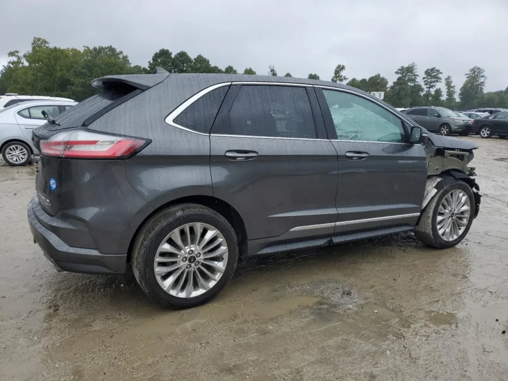 Szary Ford Edge Titanium z uszkodzonym przodem, widok z boku w deszczu