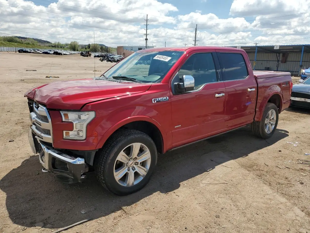 Czerwony Ford F-150 Platinum zaparkowany na żwirowym placu, widok z przodu i boku, w tle wzgórza i drzewa