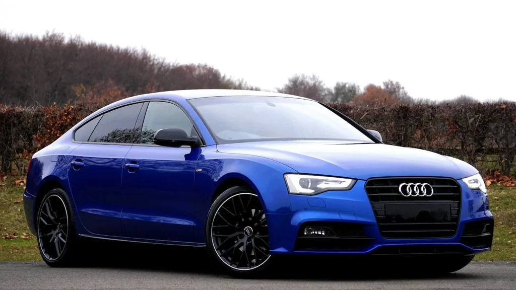 Niebieskie Audi A5 Sportback zaparkowane przy drodze na tle jesiennych krzewów