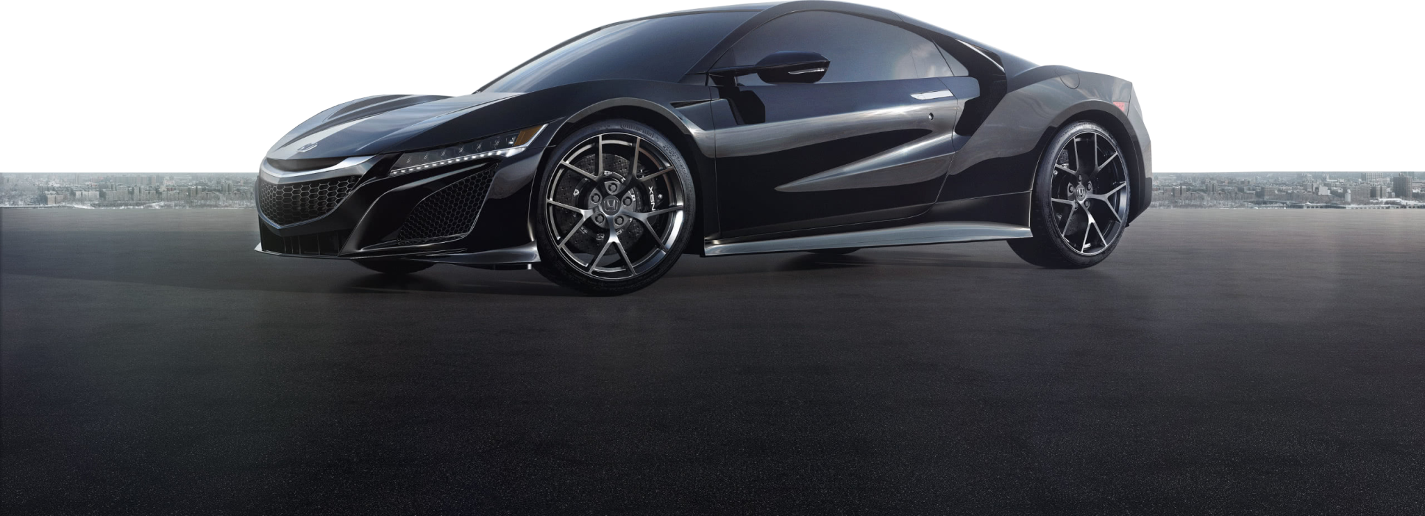 Czarna Acura NSX stoi na pustym asfalcie z panoramą miasta w tle