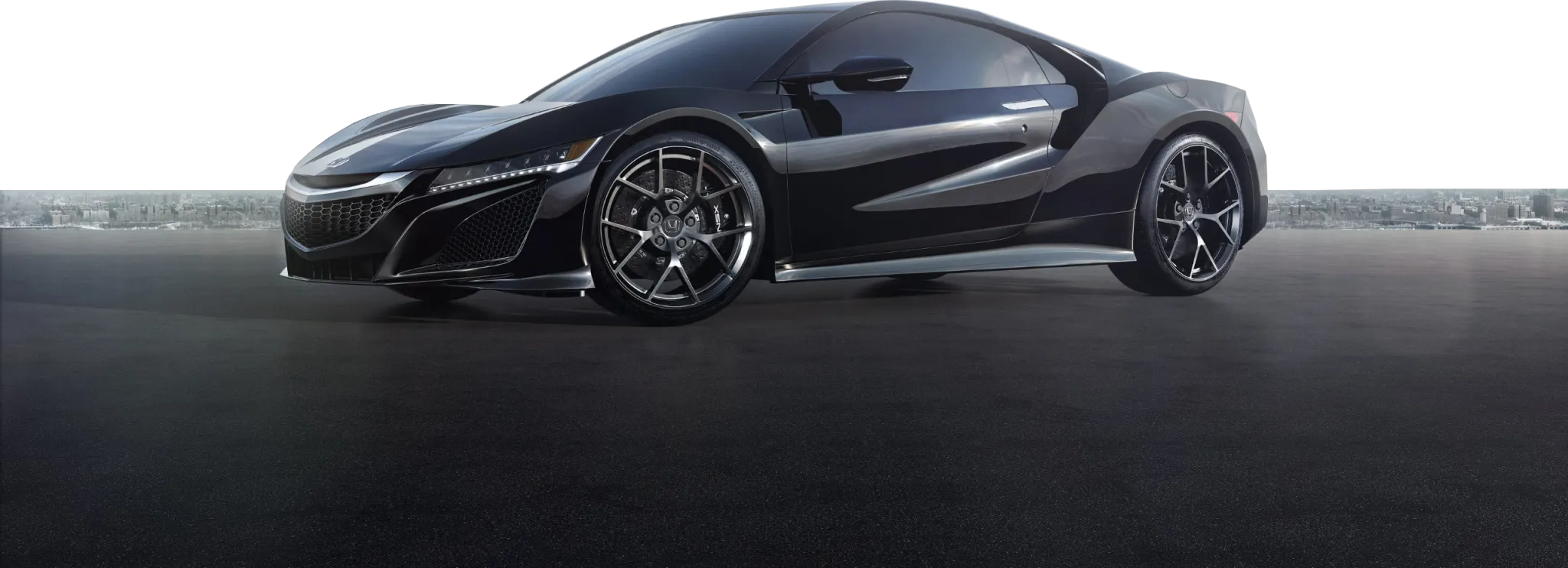Czarna Acura NSX stoi na pustym asfalcie z panoramą miasta w tle