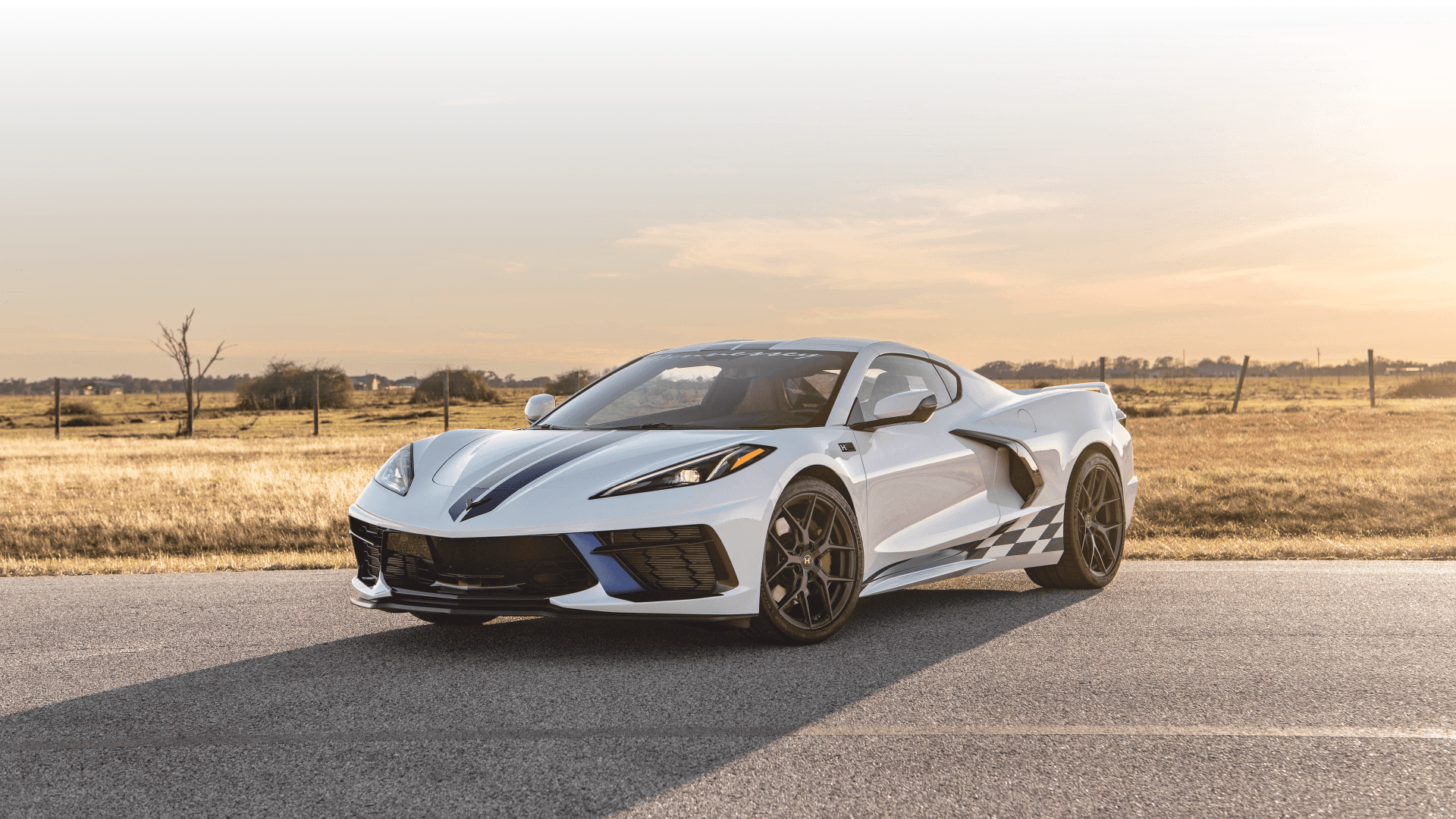 Biała Corvette C8 z niebieskimi pasami stoi na wiejskiej drodze o zachodzie słońca