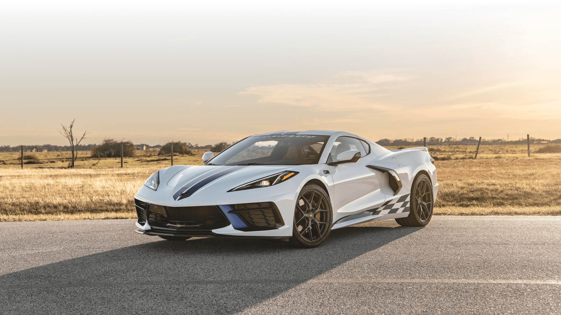 Biała Corvette C8 z niebieskimi pasami stoi na wiejskiej drodze o zachodzie słońca