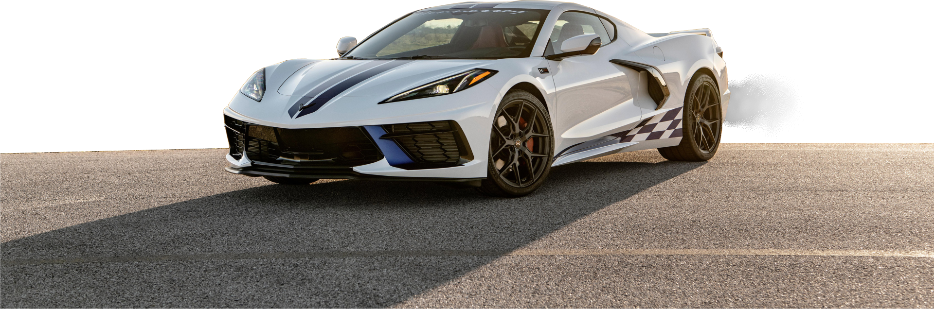 Biały Chevrolet Corvette z pasami wyścigowymi rusza na torze, z dymem za tylnym kołem.