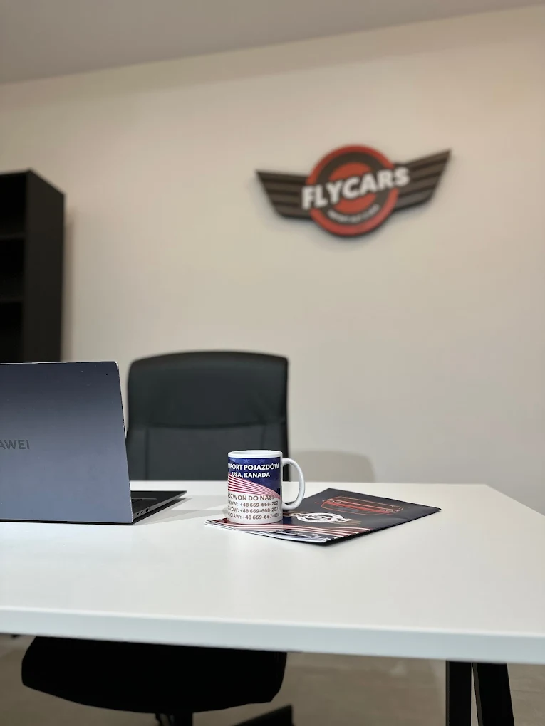 Biurko FlyCars z laptopem, kubkiem i ulotkami w biurze importu pojazdów