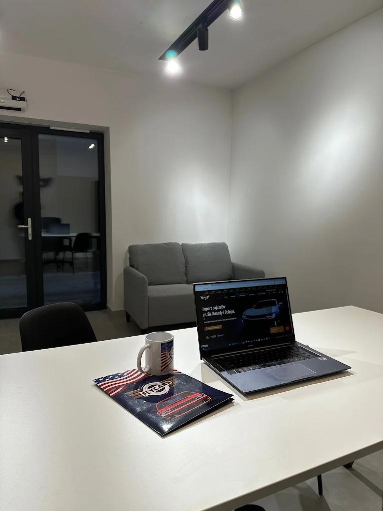 Laptop i kubek na białym stole w nowoczesnym biurze z sofą i oświetleniem sufitowym