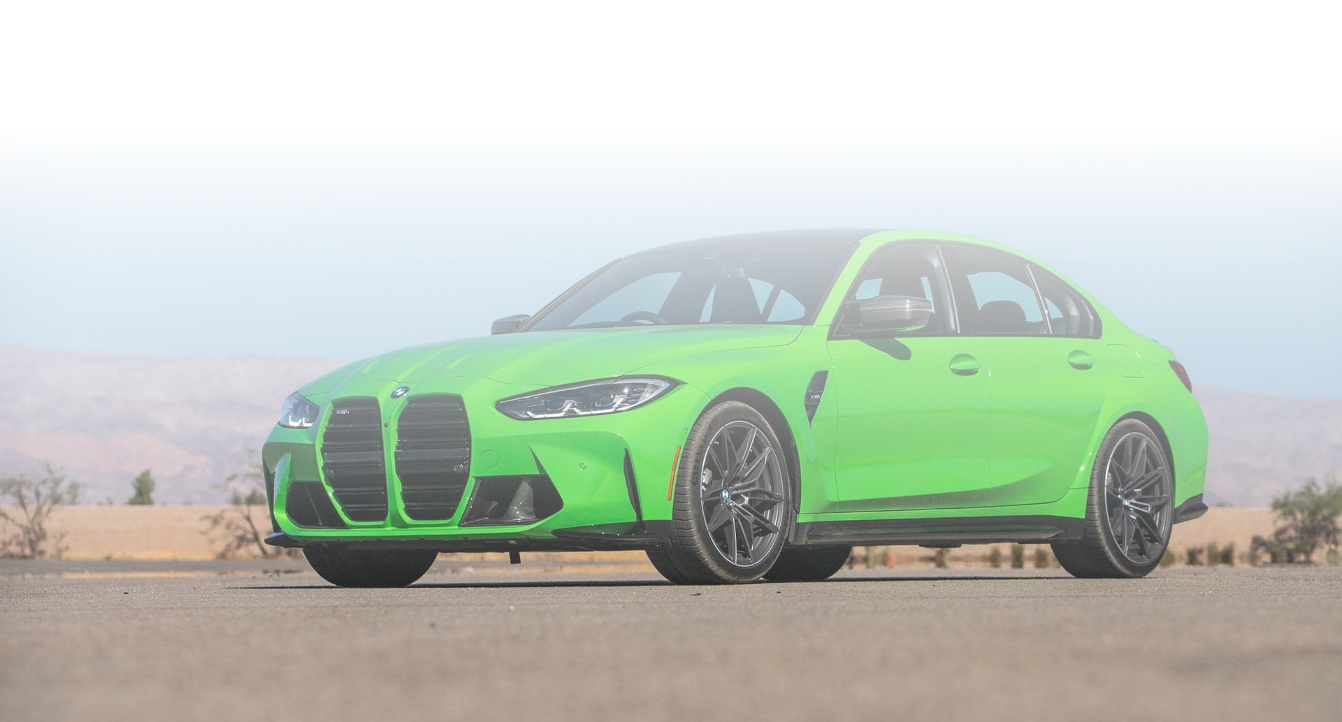 Zielone BMW M3 zaparkowane na pustynnej drodze z górami w tle