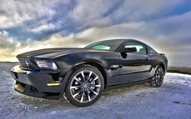 Czarny Ford Mustang GT stoi na zaśnieżonej drodze pod burzowym niebem