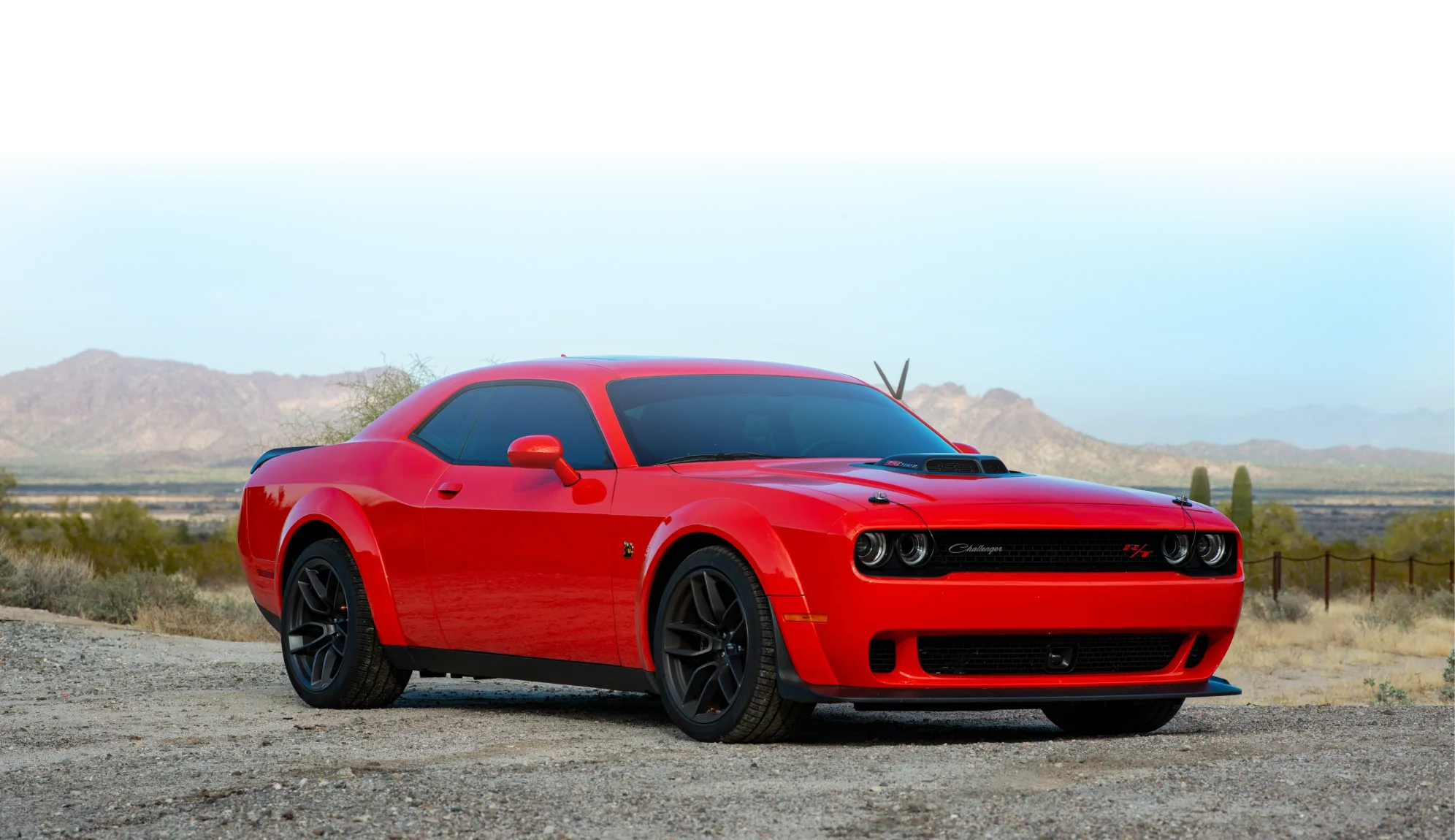 Czerwony Dodge Challenger zaparkowany na pustynnej drodze z górami w tle