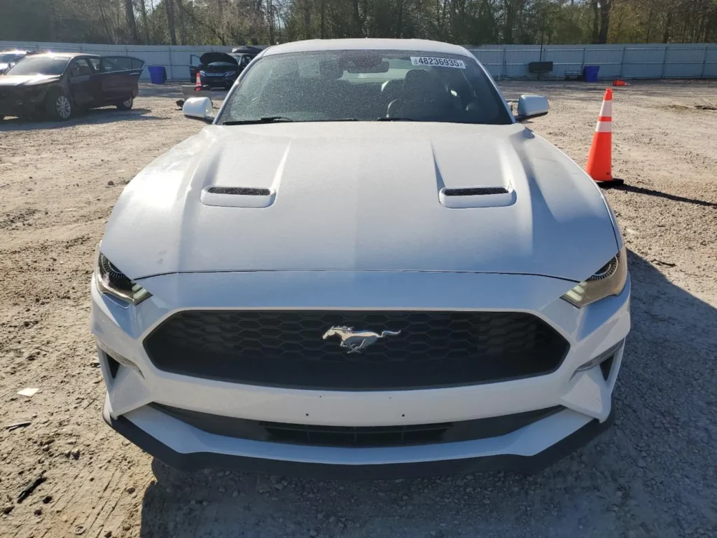 Biały Ford Mustang widziany z przodu na placu aukcyjnym z pachołkiem obok