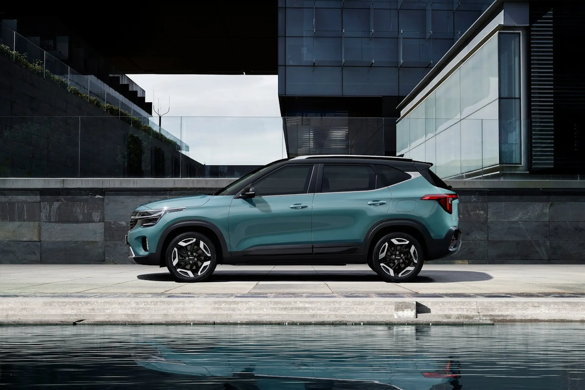 Turkusowy SUV Kia Sportage zaparkowany przed nowoczesnym budynkiem nad wodą