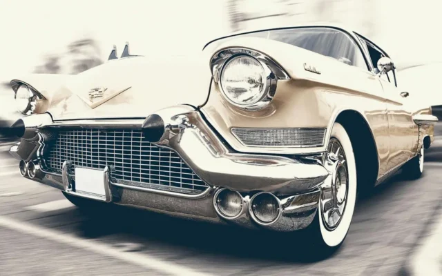 Klasyczny kremowy Cadillac jedzie ulicą, z chromowanym grillem i rozmytym tłem podkreślającym ruch.
