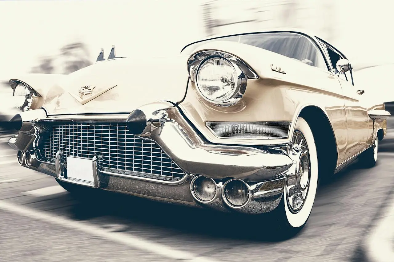 Klasyczny kremowy Cadillac jedzie ulicą, z chromowanym grillem i rozmytym tłem podkreślającym ruch.