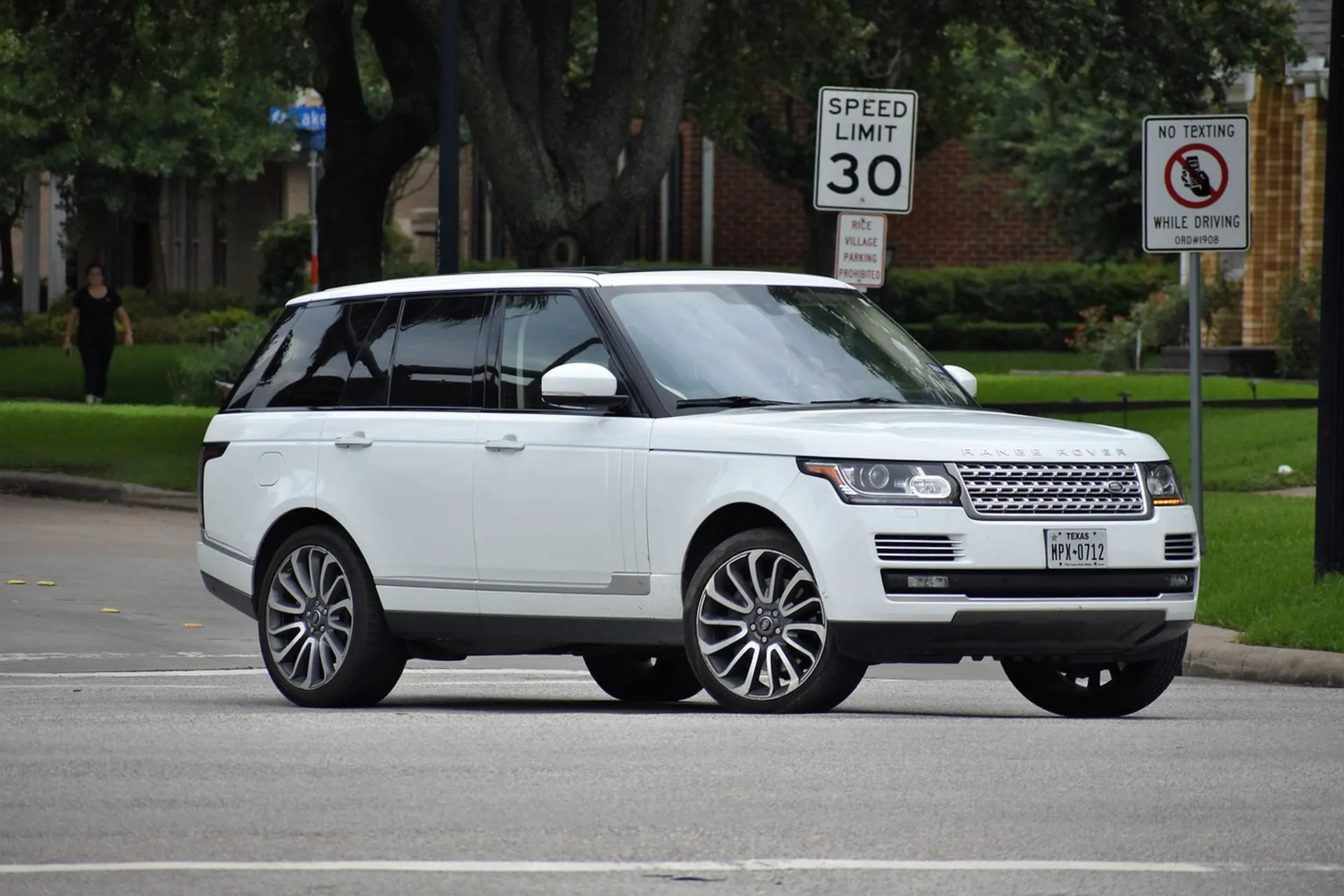 Biały SUV Range Rover na miejskiej ulicy obok znaków ograniczenia prędkości i zakazu pisania podczas jazdy