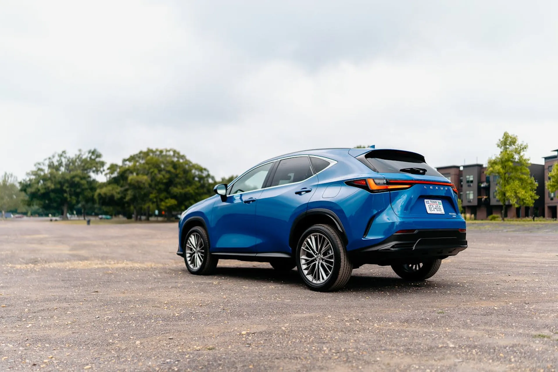 Niebieski Lexus NX stojący na żwirowym placu w miejskiej scenerii