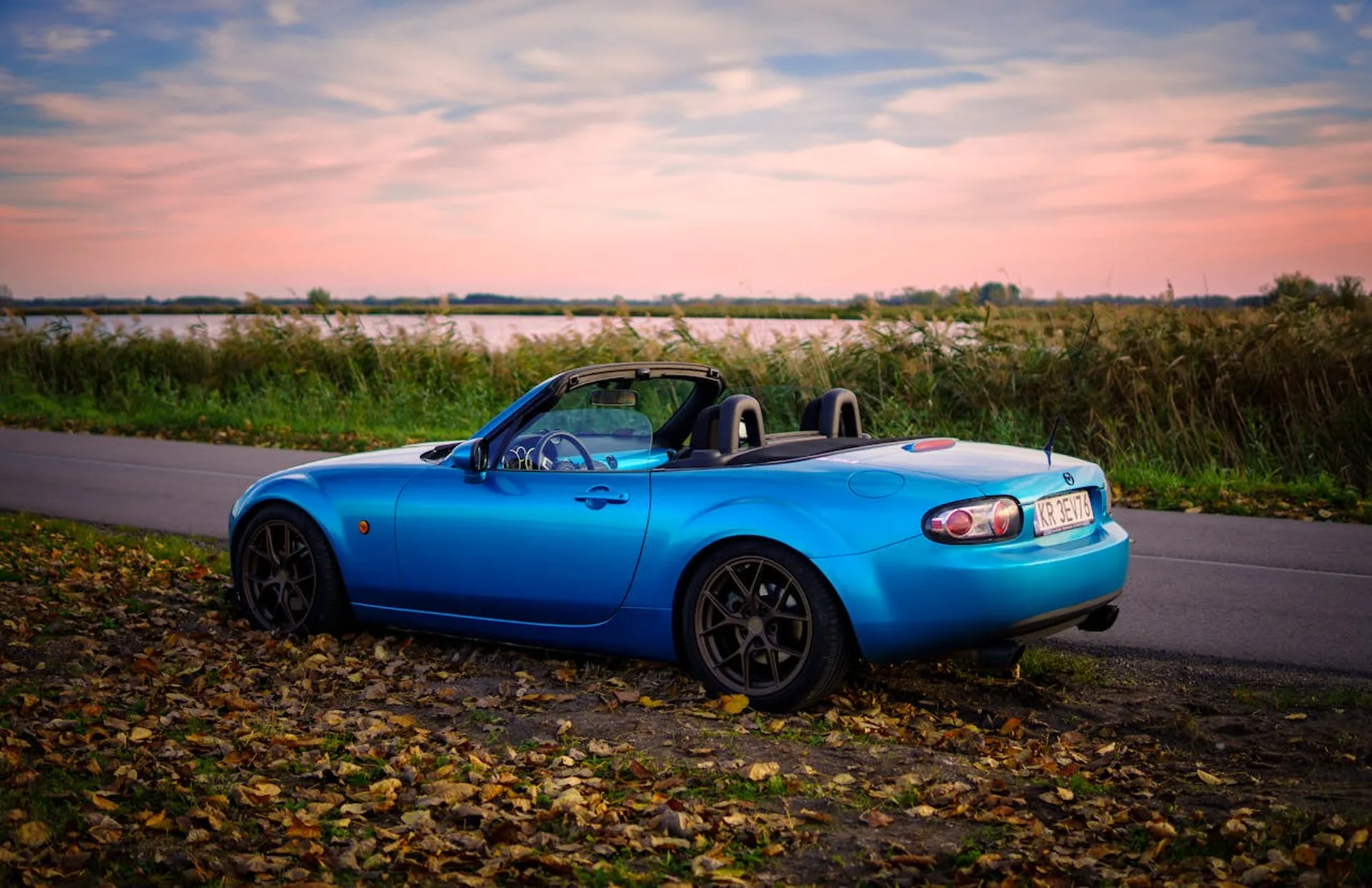 Niebieska Mazda MX-5 kabriolet zaparkowana nad jeziorem o zachodzie słońca