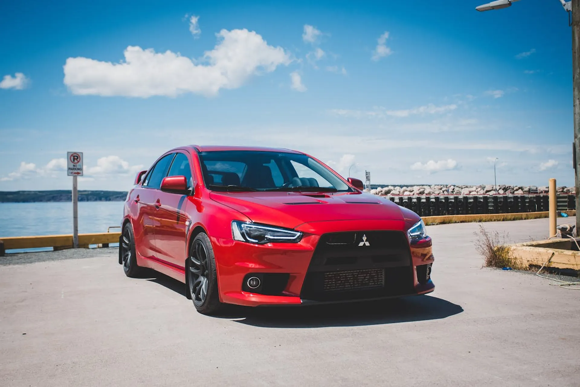 Czerwony sportowy Mitsubishi Lancer zaparkowany nad wodą w słoneczny dzień