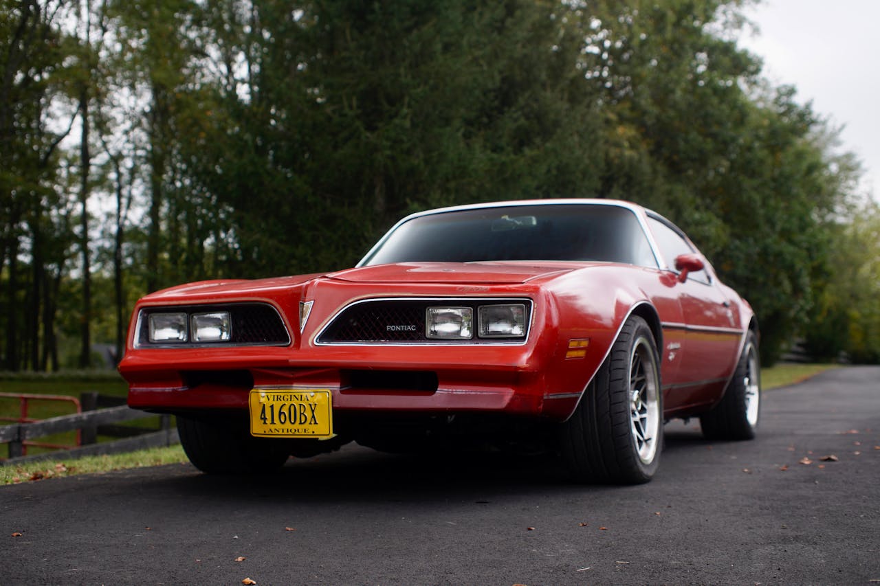 Czerwony klasyczny Pontiac Firebird zaparkowany na asfaltowej drodze w otoczeniu drzew.