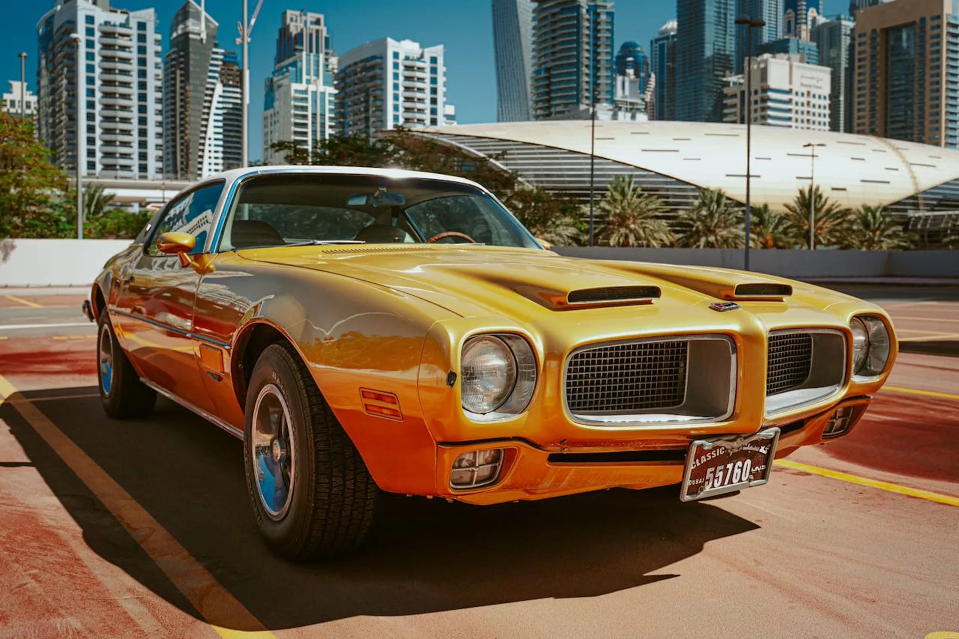 Klasyczny złoty Pontiac zaparkowany na ulicy w Dubaju, na tle wieżowców i centrum kongresowego.