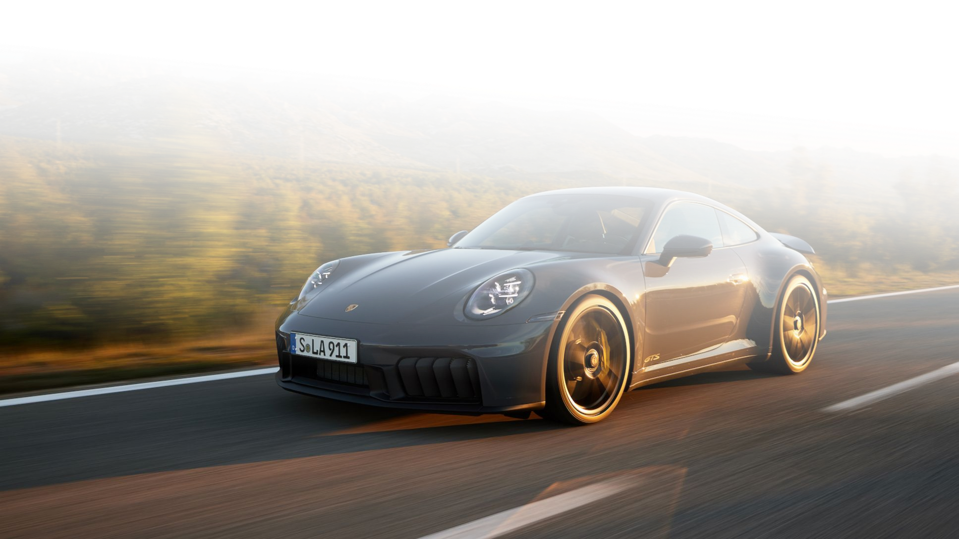 Porsche 911 GTS jedzie szybko górską drogą o zachodzie słońca, z rozmytym krajobrazem w tle