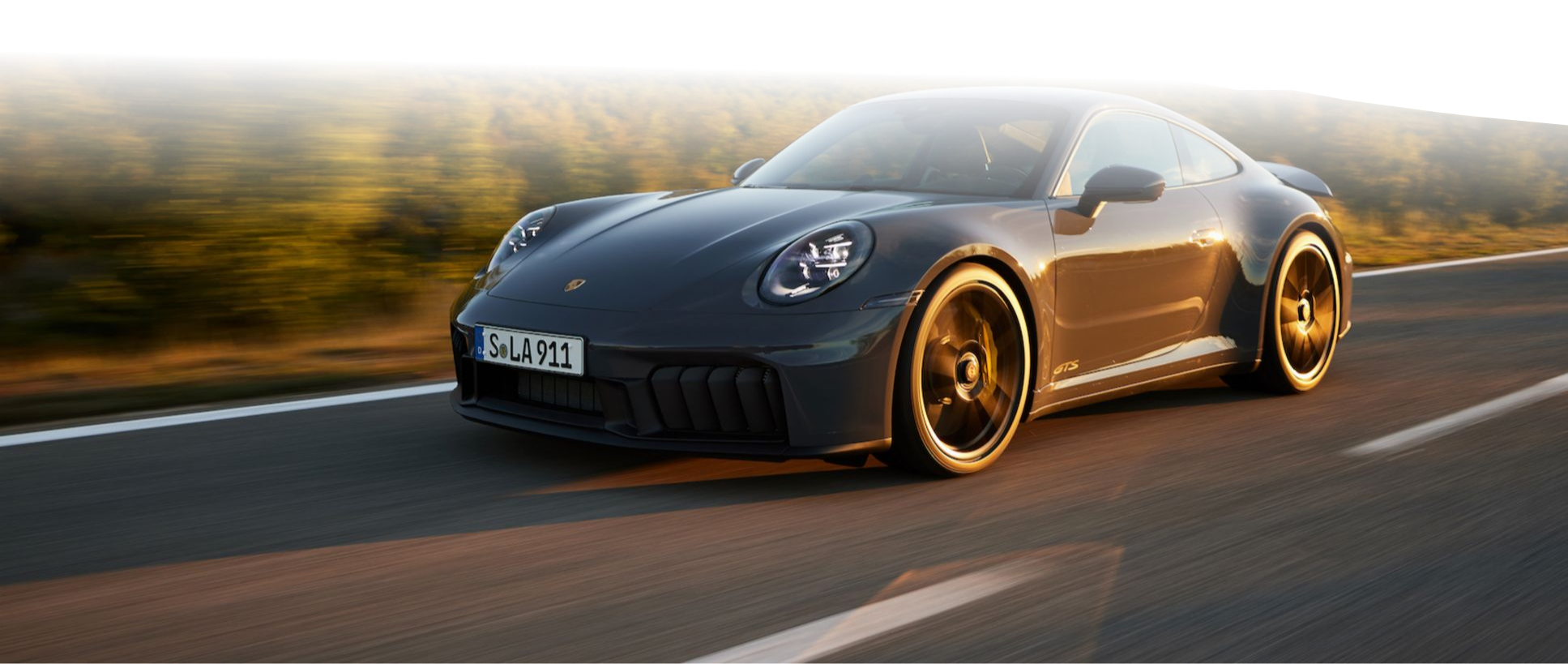 Szare Porsche 911 GTS jedzie szybko po drodze o zachodzie słońca