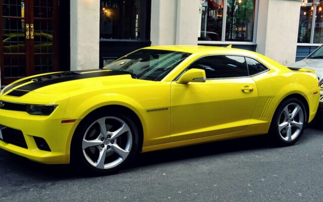 Żółty Chevrolet Camaro zaparkowany przy miejskiej ulicy przed eleganckim budynkiem
