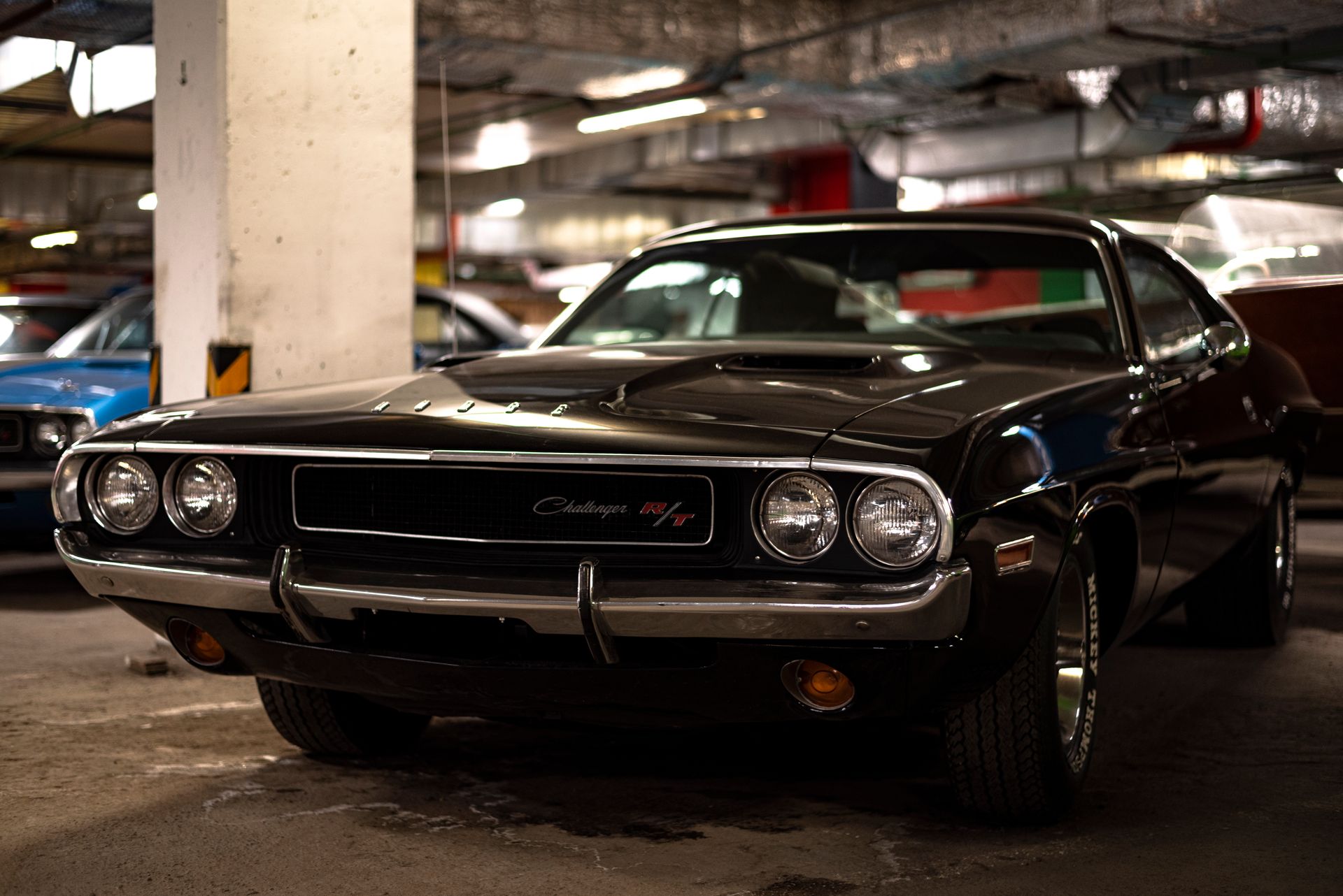 Czarny klasyczny Dodge Challenger R/T zaparkowany w podziemnym garażu, obok widoczny niebieski samochód.