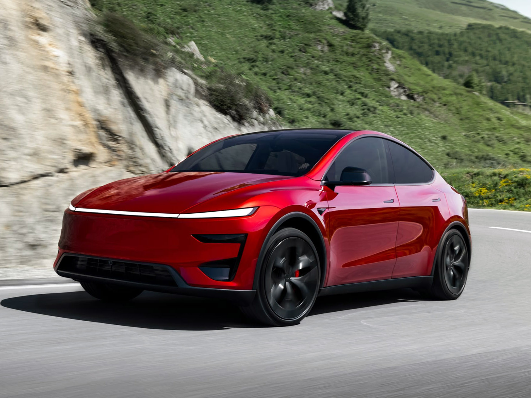 Czerwony elektryczny SUV Tesla Model Y jedzie górską drogą wśród zielonych zboczy.